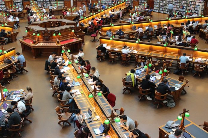 Eine große Bibliothek, in der zahlreiche Menschen an Schreibtischen arbeiten