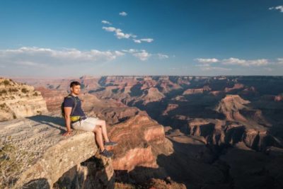 Ein junger Mann sitzt am Rande eines Felsens des Grand Canyons.