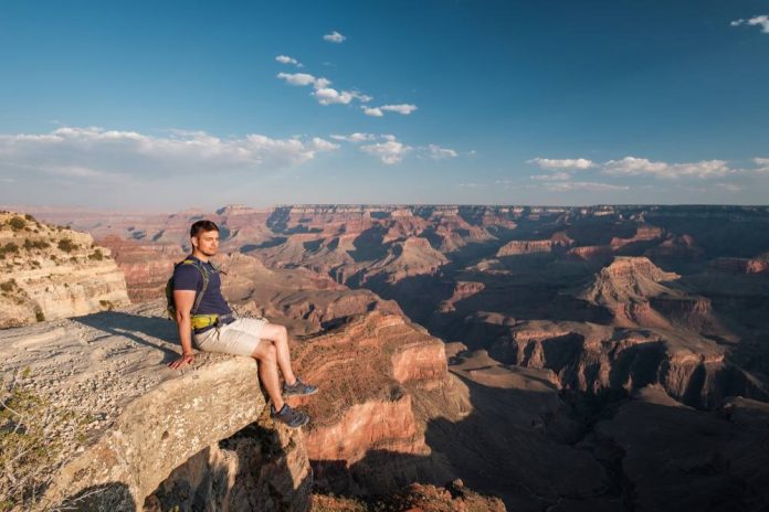 USA entdecken Ein junger Mann sitzt am Rande eines Felsens des Grand Canyons.
